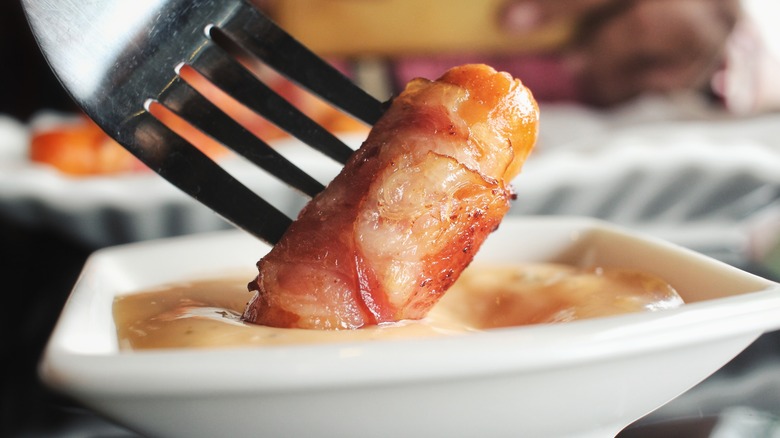 Saucisse cocktail enveloppée de bacon trempée à la fourchette dans une trempette