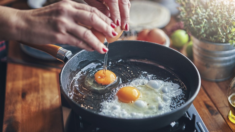 Mains faisant frire des œufs dans une poêle