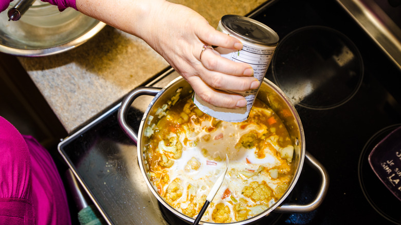 Cuisinière à domicile ajoutant une boîte de lait évaporé à la soupe