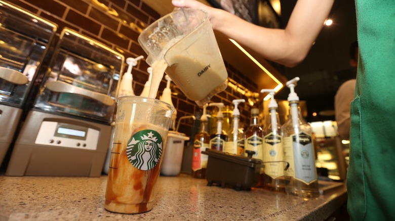 Un barista de Starbucks verse du lait dans une boisson glacée au caramel