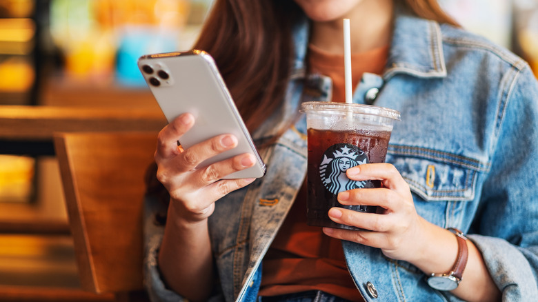 Personne tenant un téléphone et un café glacé