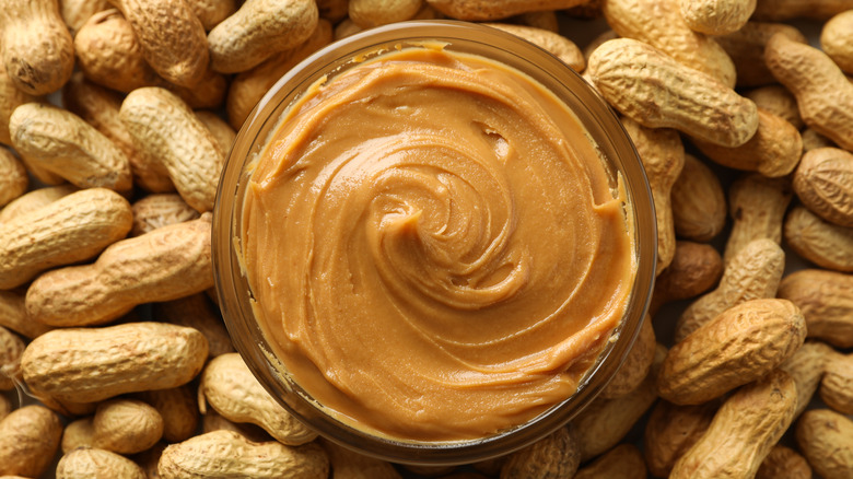 Beurre de cacahuète dans un bol entouré de cacahuètes