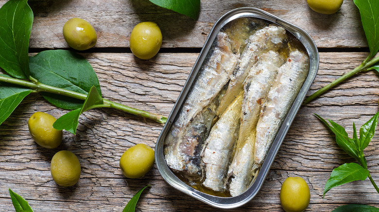 sardines en conserve emballées dans de l'huile avec des feuilles d'olivier sur une table en bois