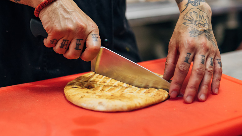 Gros plan des mains qui coupent du pain pita