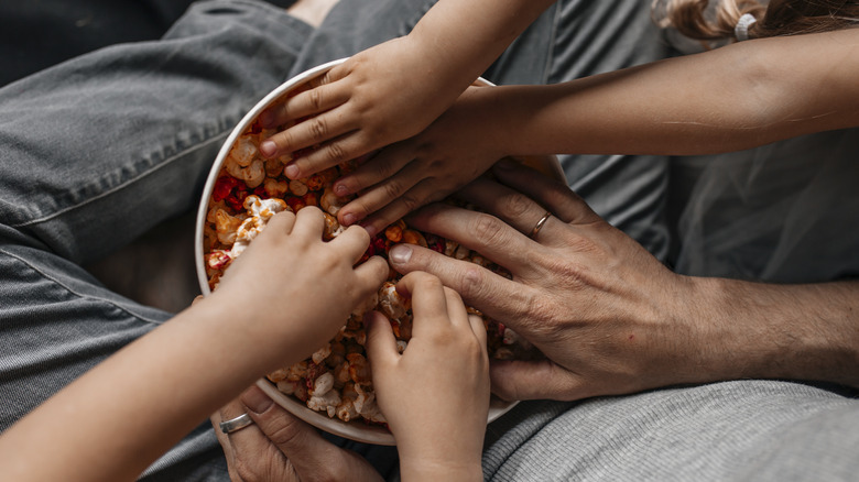 Les mains de plusieurs personnes plongeant dans un bol de pop-corn aromatisé