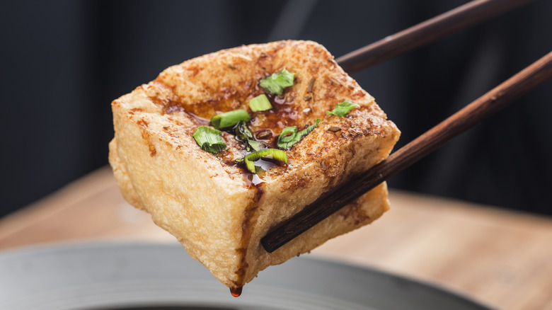 Des baguettes ramassent du tofu frit avec des oignons verts et de la sauce