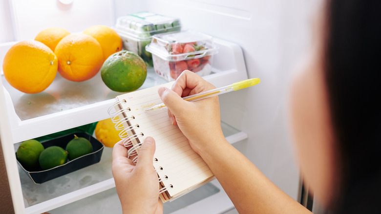 Femme prenant des notes devant un réfrigérateur 