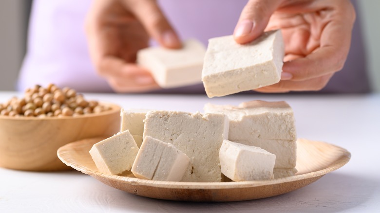 Tranches de tofu sur une assiette en bois avec la main