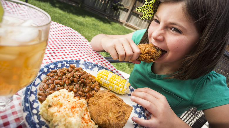 Une jeune fille mangeant du poulet frit lors d'un pique-nique