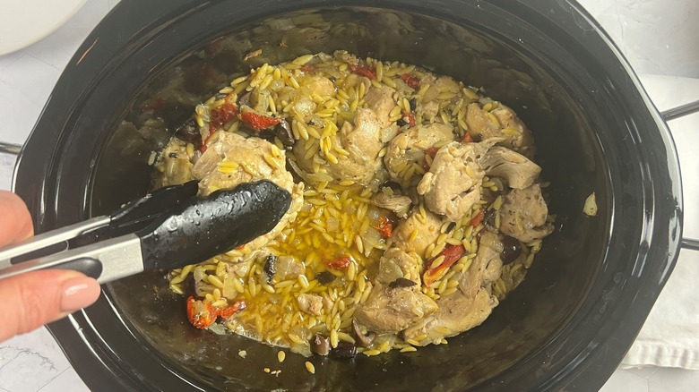 main tenant du poulet avec des pinces au-dessus d'un pot d'orzo