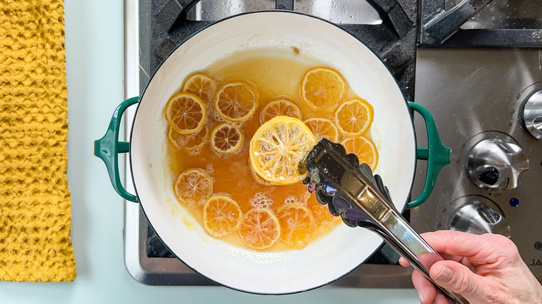 Rondelles de citron confites au sirop dans une casserole sur la cuisinière avec des pinces