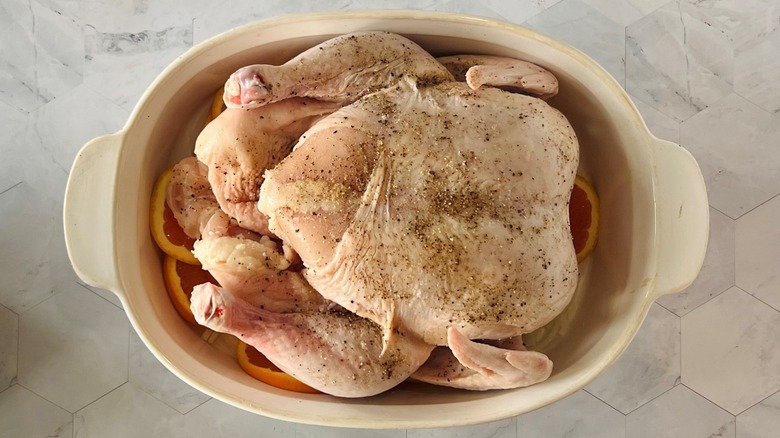 poulet cru dans un plat allant au four sur des oranges et des oignons