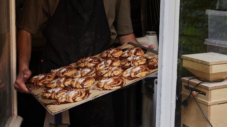 personne tenant un plateau de kanelbullar avec pärlsocker