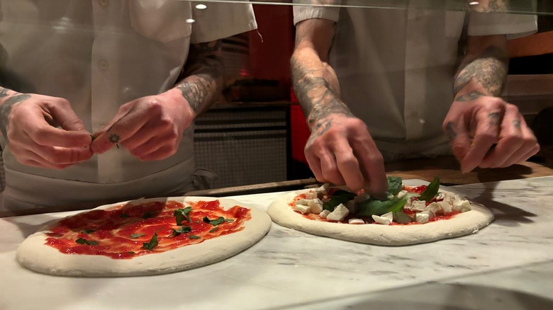 Des chefs garnissent des pizzas