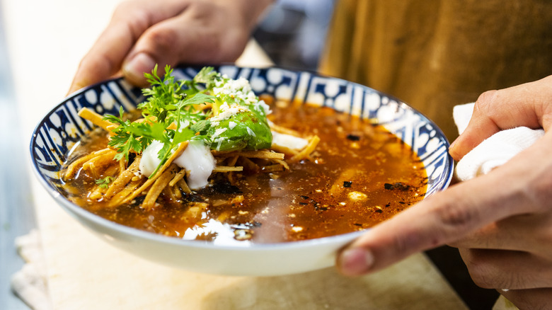 Mains tenant un bol de soupe aux tortillas